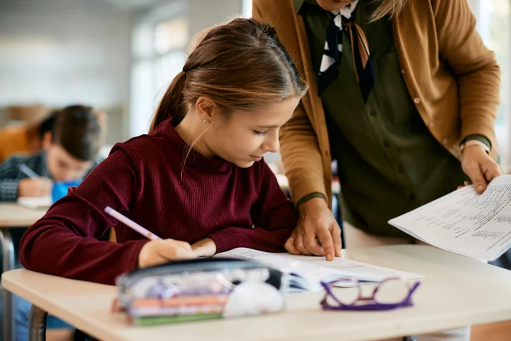 A young student reading and writing at a desk with help from a mentor